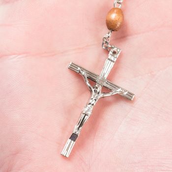 Silver cross of rosary beads in palm of hand