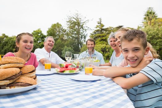 Extended family having dinner outdoors at picnic table smiling at camera