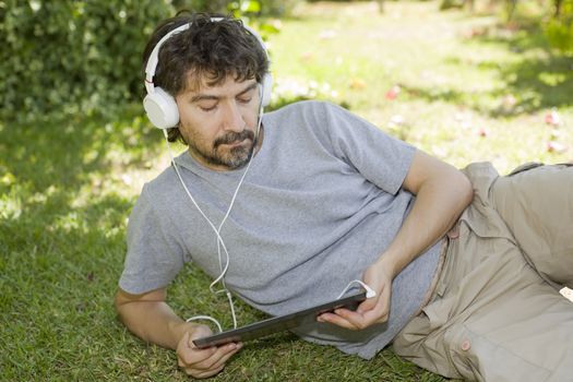 young man holding a tablet with headphones, outdoor