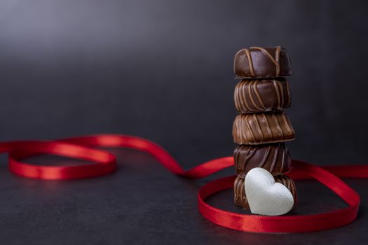Stack of Chocolate candy and red ribbon on a black background. Focus on chocolates