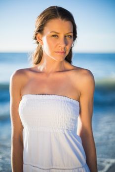 Serious brunette in white summer dress posing on the beach at dusk