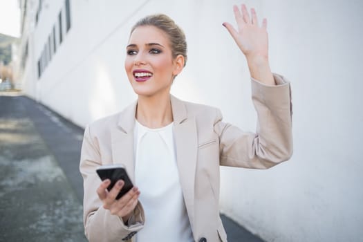 Cheerful attractive businesswoman waving outdoors on urban background