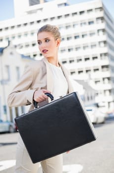Serious elegant businesswoman holding briefcase outdoors on urban background