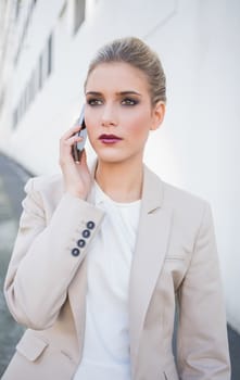Thoughtful attractive businesswoman on the phone outdoors on urban background