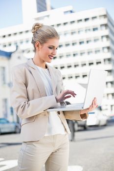 Cheerful elegant businesswoman working on laptop outdoors on urban background