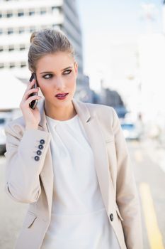 Pensive gorgeous businesswoman having a phone call outdoors on urban background
