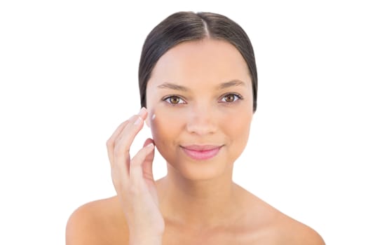 Smiling woman spreading beauty cream on her cheek against white background