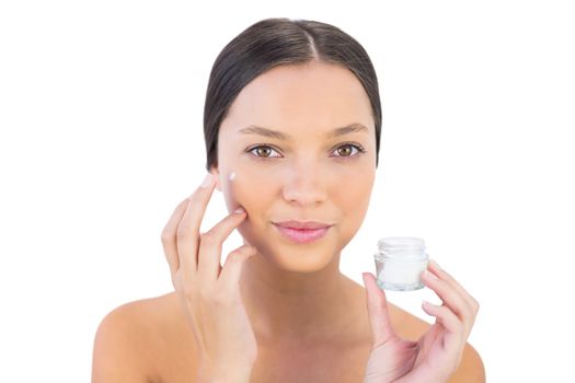 Attractive woman spreading beauty cream on her cheek against white background