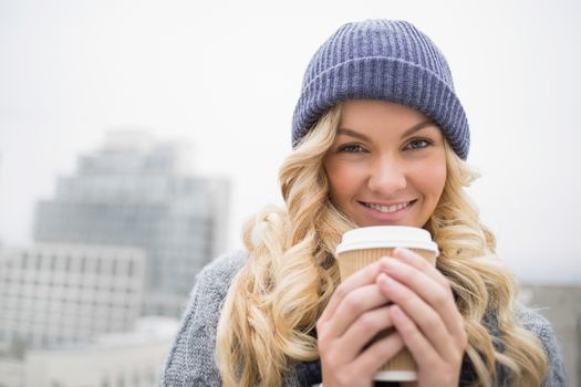 Cheerful pretty blonde having coffee outdoors on urban background