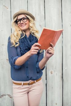 Cheerful fashionable blonde holding book outdoors on wooden background