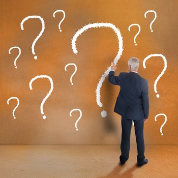 Mature businessman touching question mark on beige wall