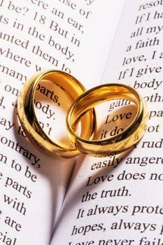 Two golden wedding rings on Holy bible book with heart shaped shadow close up