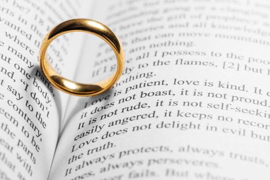 One golden wedding ring on Holy bible book with heart shaped shadow close up