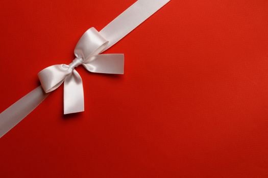 White satin ribbon bow on red paper background