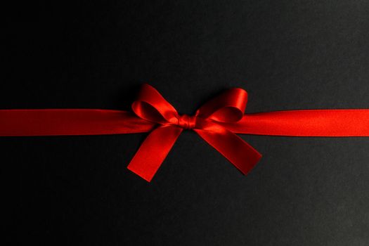 Red satin ribbon bow on black paper background