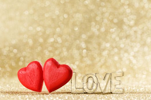 Two red handmade wooden hearts and word love on golden bright glitter lights bokeh background