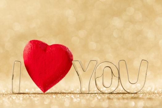 Red handmade wooden heart in I LOVE YOU sign word on golden bright glitter lights bokeh background