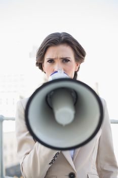 Frowning stylish brown haired businesswoman speaking in a megaphone outdoors