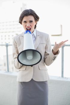 Angry stylish brown haired businesswoman yelling in a megaphone outdoors