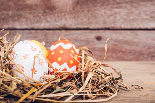 Beautiful Easter multi color egg in straw on wooden background, Easter day concept