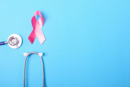 Breast cancer month concept, flat lay top view, pink ribbon and stethoscope on blue background with copy space for your text