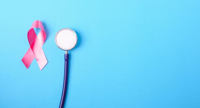 Breast cancer month concept, flat lay top view, pink ribbon and stethoscope on blue background with copy space for your text