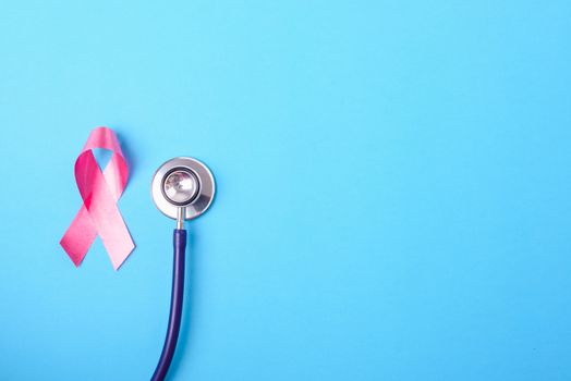 Breast cancer month concept, flat lay top view, pink ribbon and stethoscope on blue background with copy space for your text