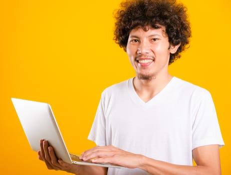Asian handsome man with curly hair using laptop computer isolate on yellow background with copy space for text