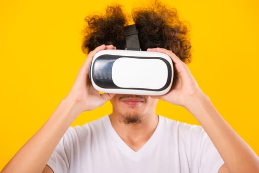 Asian handsome man with curly hair he using virtual reality headset or VR glass isolate on yellow background