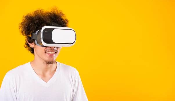 Asian handsome man with curly hair he using virtual reality headset or VR glass isolate on yellow background