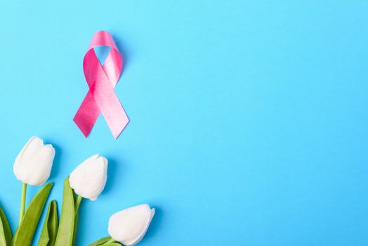 Breast cancer month concept, flat lay top view, pink ribbon and Tulip Flower on blue background with copy space for your text