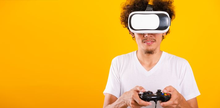 Asian handsome man with curly hair play game he using virtual reality headset or VR glass isolate on yellow background with copy space for text
