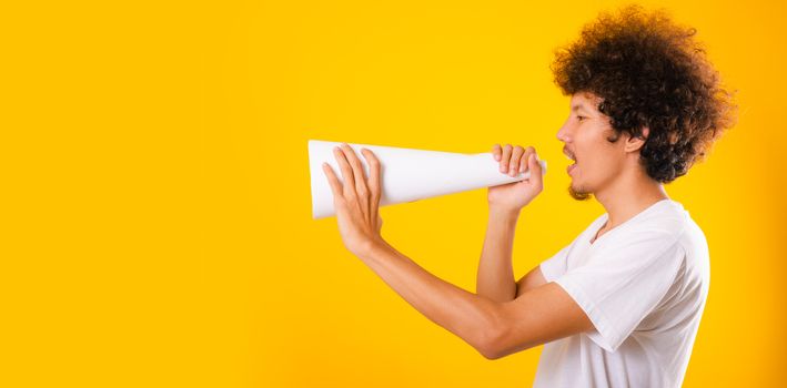 Asian handsome man with curly hair he announcing or spreading news using white speaker paper isolate on yellow background