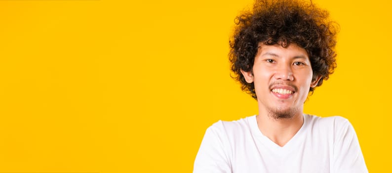 Portrait of Asian handsome man with curly hair with arms crossed isolate on yellow background with copy space for text