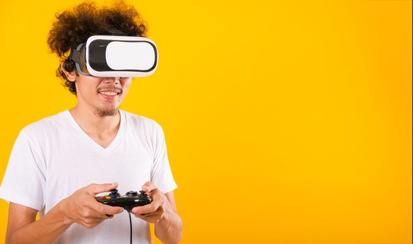 Asian handsome man with curly hair play game he using virtual reality headset or VR glass isolate on yellow background with copy space for text