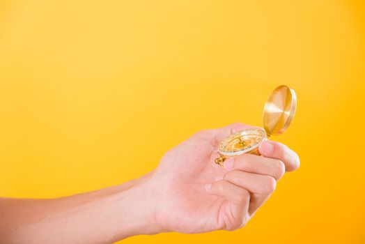 Hand holding antique brass compass isolated on yellow background with copy space for text