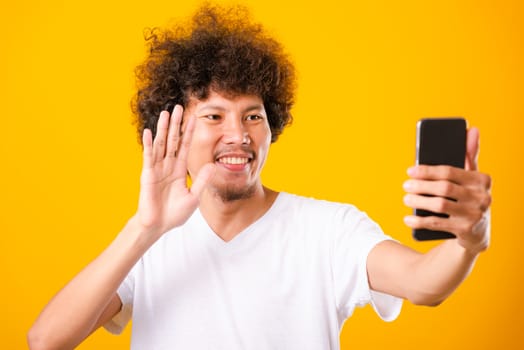 Portrait asian handsome man curly hair taking selfie with mobile phone isolated on yellow background