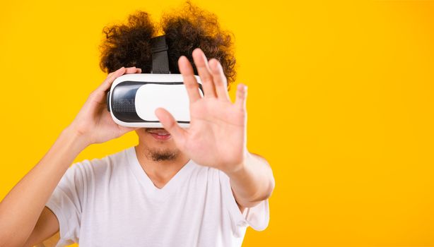 Asian handsome man with curly hair he using virtual reality headset or VR glass isolate on yellow background