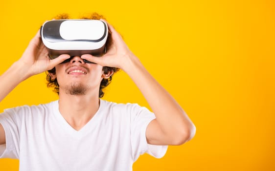 Asian handsome man with curly hair he using virtual reality headset or VR glass isolate on yellow background