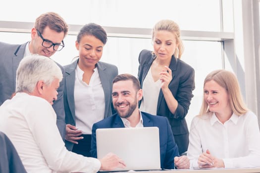 Business team sitting by the table and working smiling with laptop and documents in office