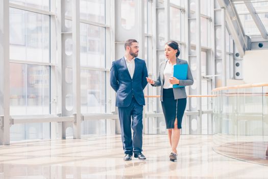 Businessman and businesswoman walk together and talk about business holding coffee in hand