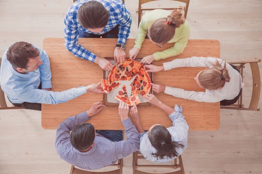 People taking pizza slices from wooden table, top view