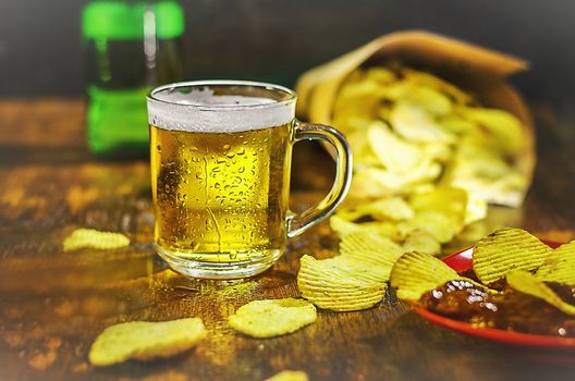 A glass of cold beer and chips on a wooden table. The concept of a football fan