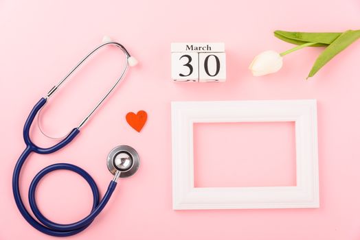 Doctor's Day concept, flat lay top view, equipment medical red heart stethoscope and photo frame on pink background, care patient in hospital with copy space for text