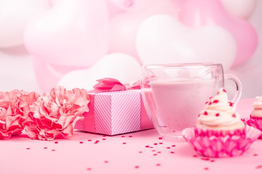 Valentine Day gift in a box wrapped in striped paper and tied with silk ribbon bow and dessert on pink balloons background with copy space for text