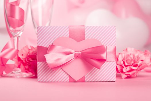 Valentine Day gift in a box wrapped in striped paper and tied with silk ribbon bow and heart shaped greeting card on pink balloons background with copy space for text