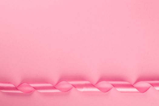 Valentine day background with pink curly satin ribbon on pink paper with copy space for text