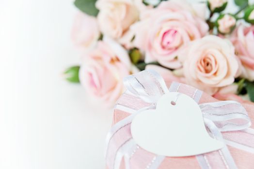 Gift box with label, ribbon and pink rose flowers on a light background