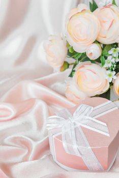 Bouquet of pink camellia flowers and gift box with bow on a background of wavy pink silk fabric; vertical image