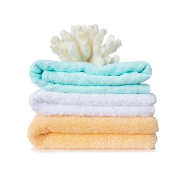 Beautiful large white sea coral on the stack of yellow, blue and white fluffy terry towels  isolated on a white background